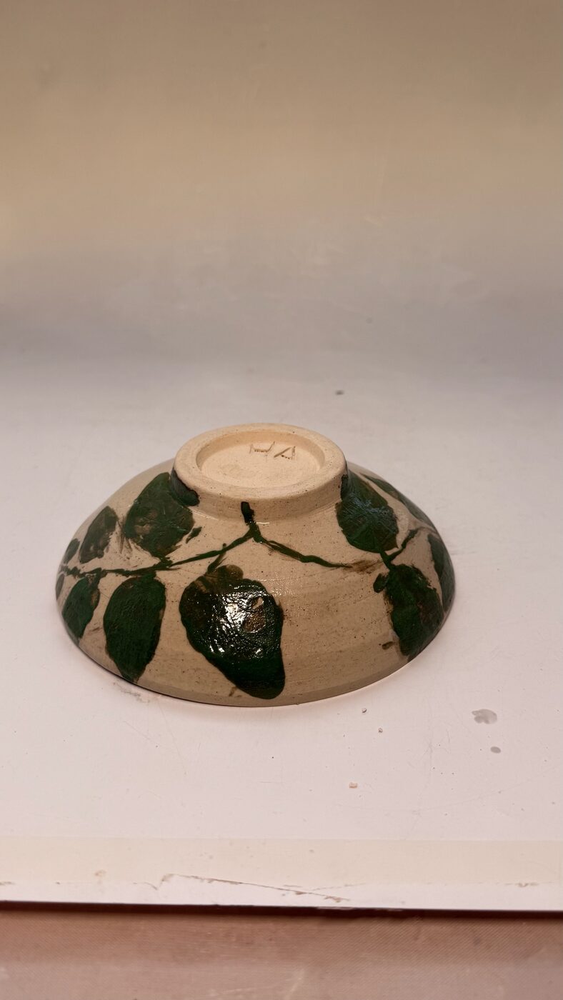 Wheel-thrown footed bowl with green leaf imagery under a matte cream glaze