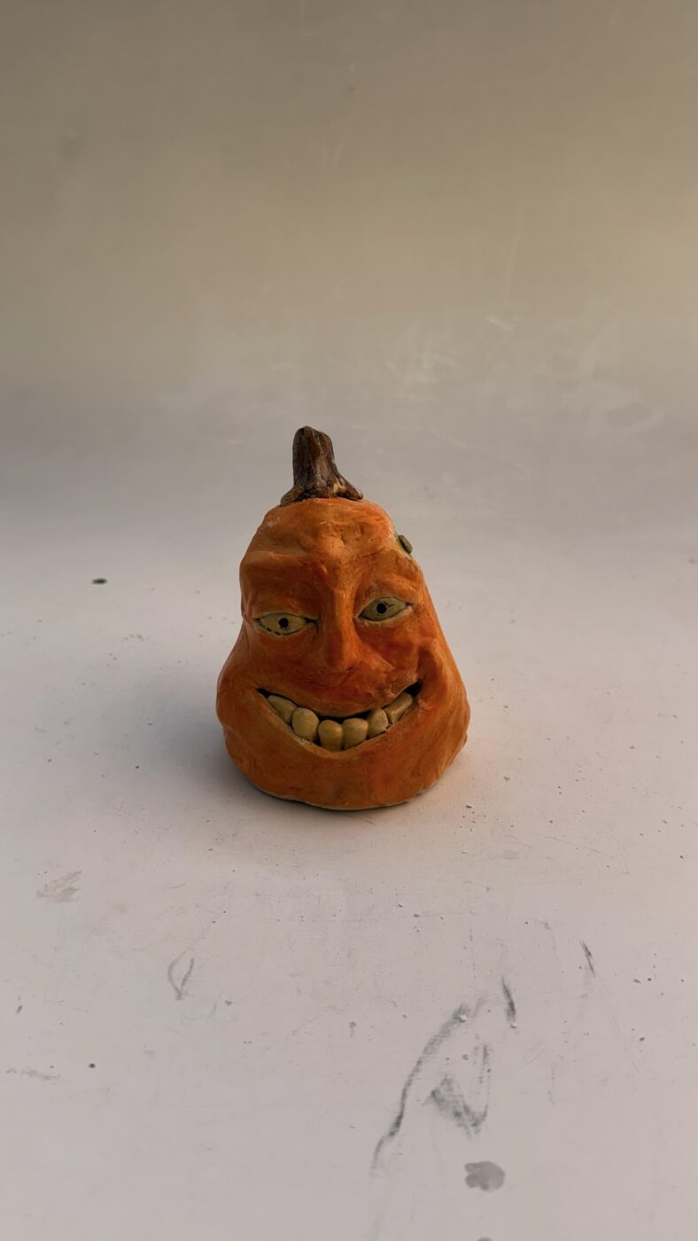 Hand-built ceramic pumpkin with a sculpted smiling face and orange underglaze