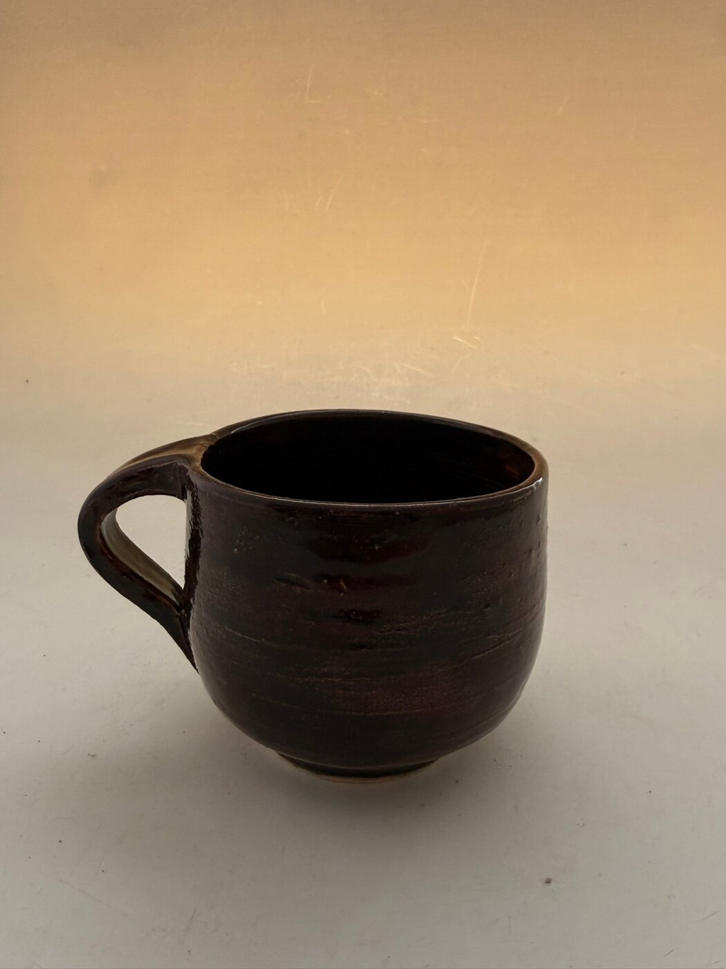 Wheel-thrown mug with a deep brown celadon glaze and pulled handle