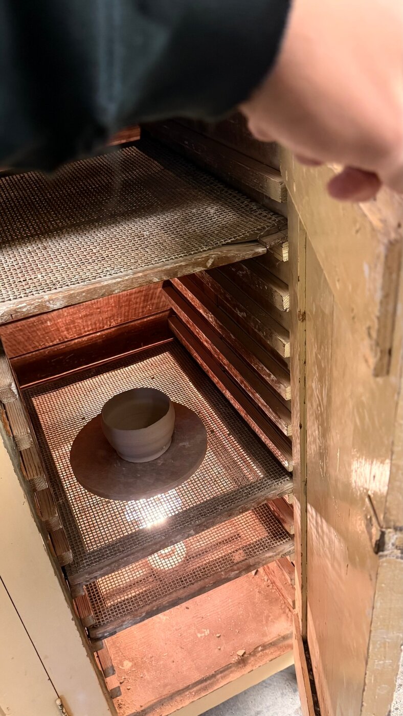 Small wheel-thrown cup drying on a bat in the studio drying rack